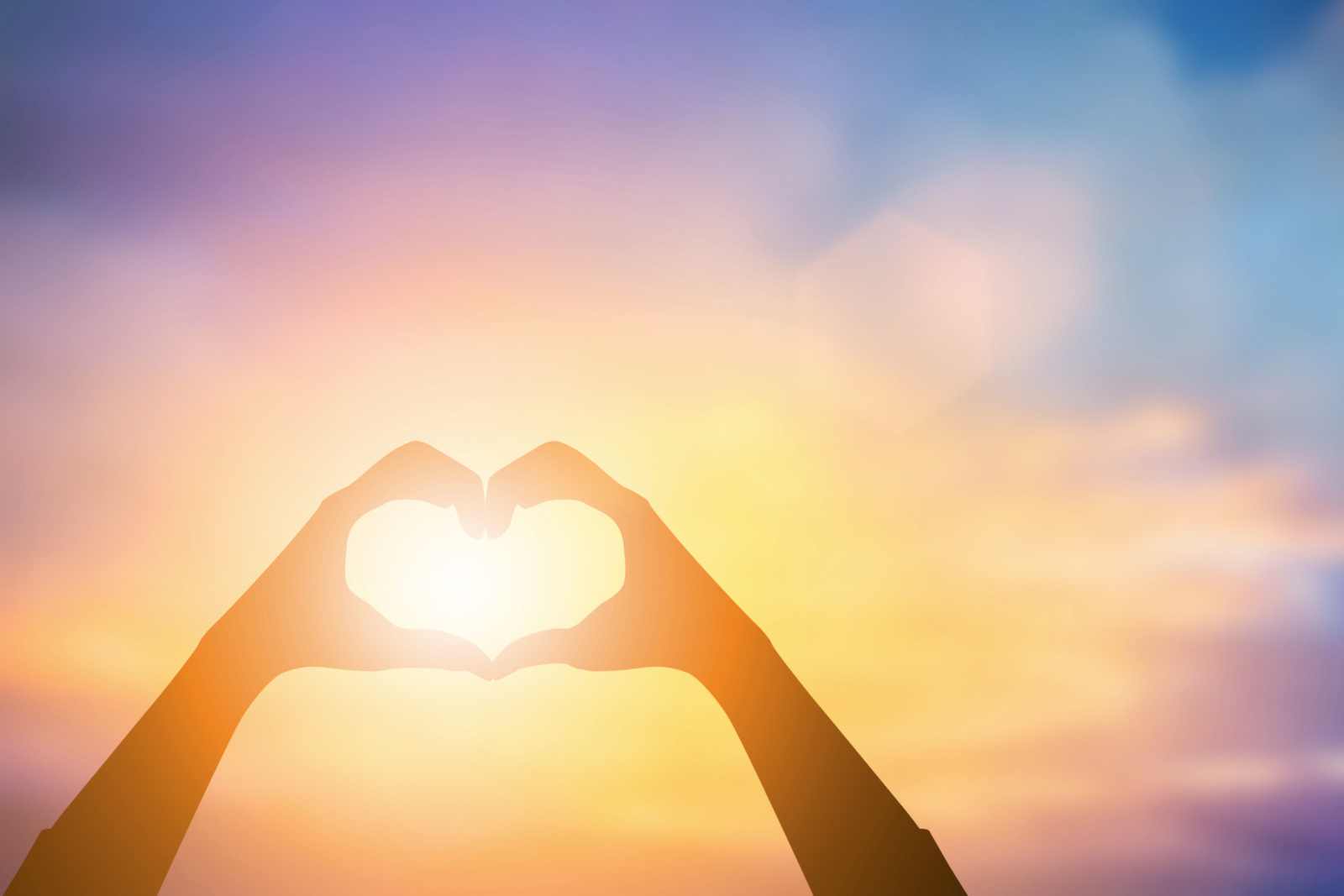 Hands forming heart shape against rising sun,